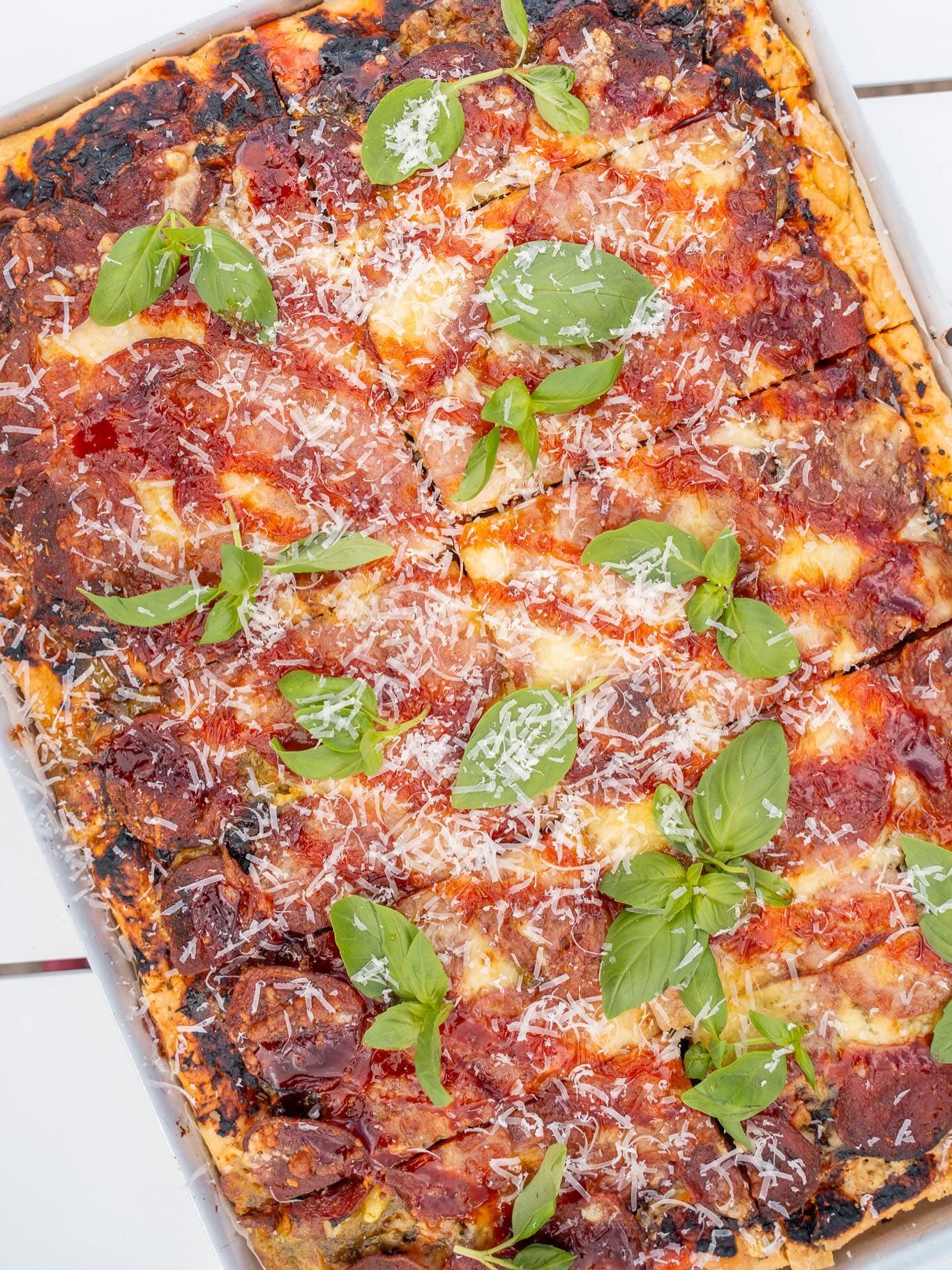 Detroit-style pan pizza with basil and shredded parmesan